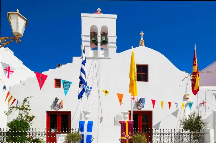 A Greek Orthodox church adorned with colorful flags above a narrow alley in Mykonos Town, Mykonos Island, Greece