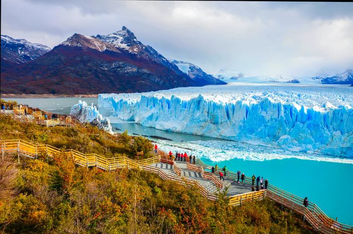 Visitors stand on a platform overlooking a striking blue and white glacier.