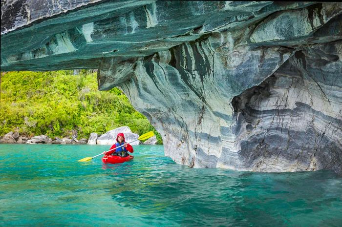 A kayaker transitions from vibrant turquoise waters into a cave adorned with grey and white streaked rocks.