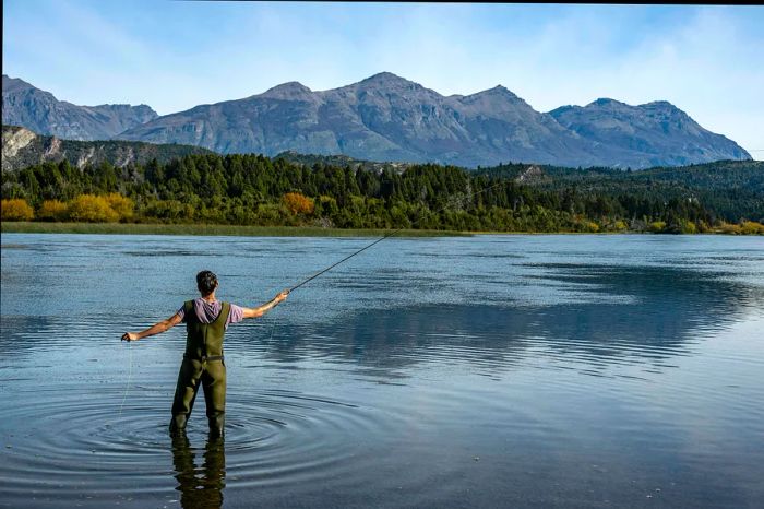 A man fly-fishing in a river surrounded by hills