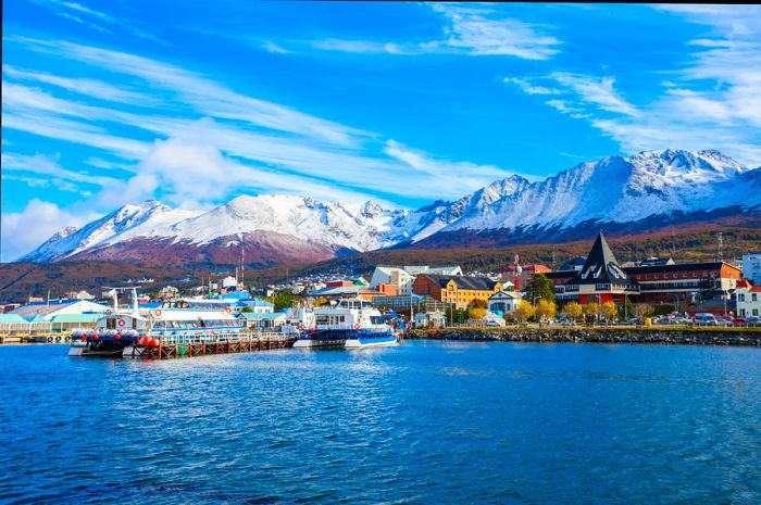 Boats line the harbor in Ushuaia, Argentina, with snow-capped mountains rising in the background.