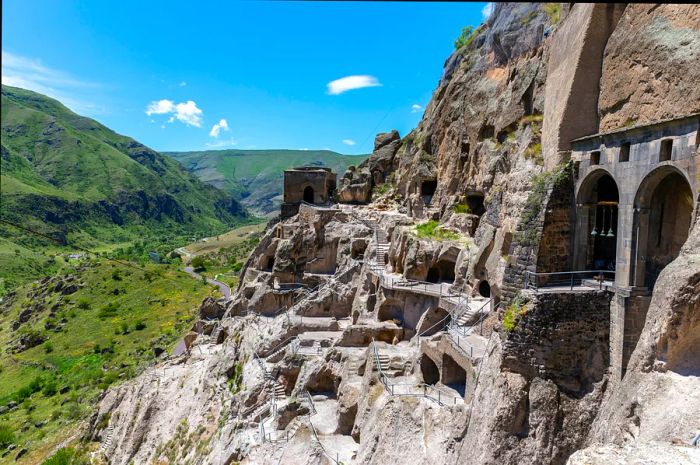 A rocky escarpment featuring caves, tunnels, and homes carved into the stone, with a river valley visible in the background.