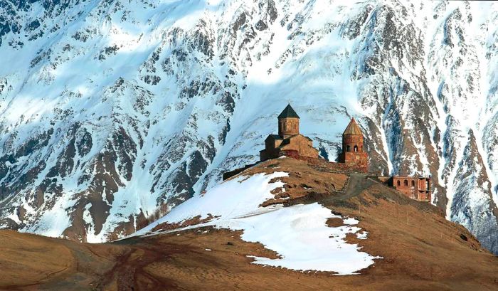 A monastery in Georgia perched on a hill, with breathtaking snowy mountains in the background.