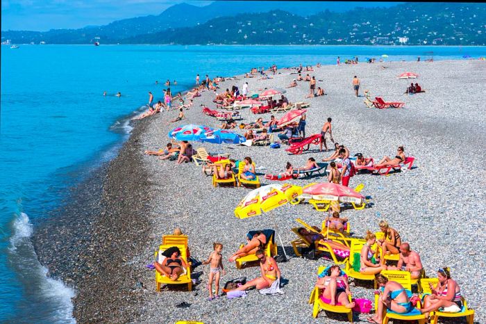 A bustling crowd enjoys a sunny day on a pebble beach