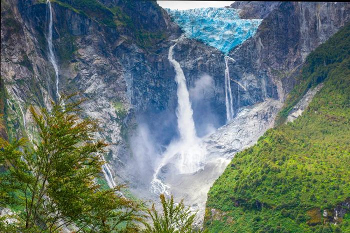 A glacier perched on a rocky face with a waterfall flowing down