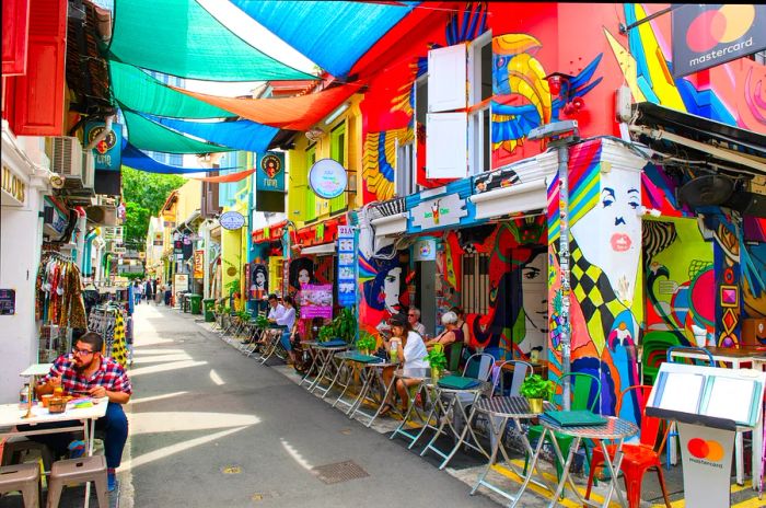 Diners enjoy meals at outdoor tables on a vibrant street adorned with colorful decor.