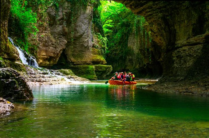 A group of people paddling a raft down a blue-green river in a canyon