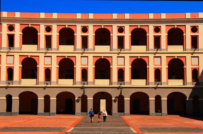 Visitors walking toward the Museo de las Américas in San Juan, Puerto Rico, a striking three-story structure adorned with arches.