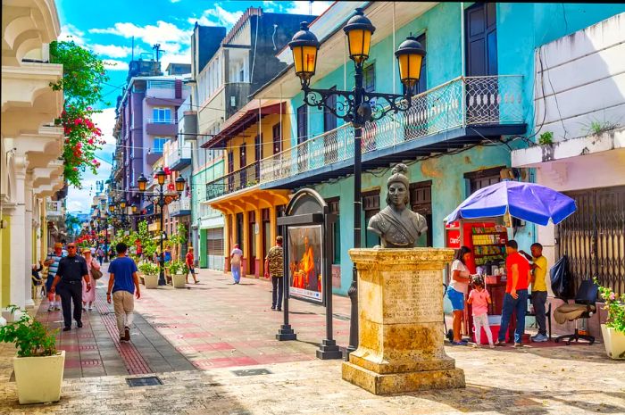 A bronze bust of a woman graces one end of a pedestrian-friendly street lined with historic architecture.