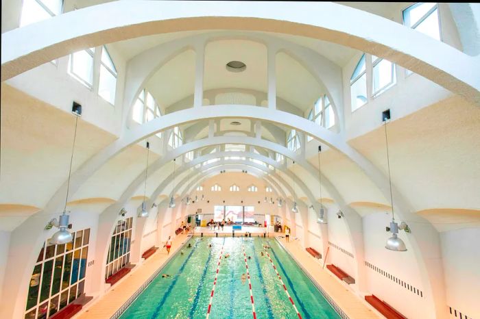 Swimmers glide back and forth in an indoor lap pool beneath elegant white arched ceilings.