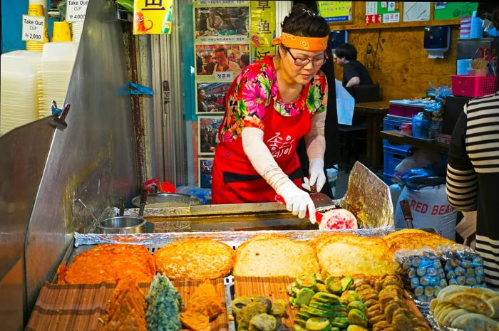 A woman vendor prepares snacks at a stall in Gwangjang Market, Seoul, South Korea.