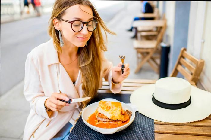 A woman enjoys a traditional Portuguese sandwich called a francesinha outdoors in Porto, Portugal