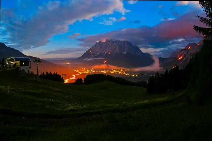 The mountains glow in shades of red and orange against the night sky, illuminated by numerous fires.