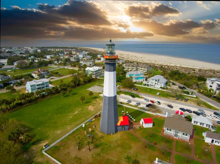 A striking black and white lighthouse stands tall over a sandy beach.