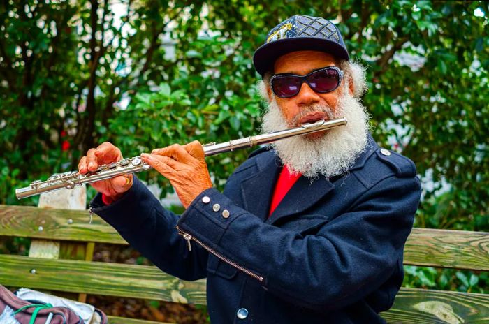 A talented black musician performs on the flute in a picturesque square within Savannah's historic district.