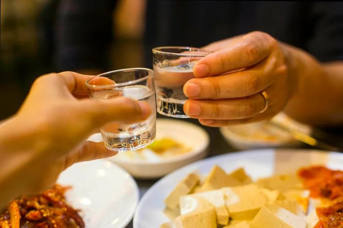 Two individuals clink glasses of soju at a restaurant in South Korea, Asia