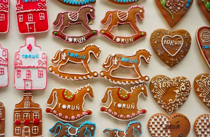 A collection of beautifully decorated gingerbread cookies shaped like rocking horses, love hearts, and houses.