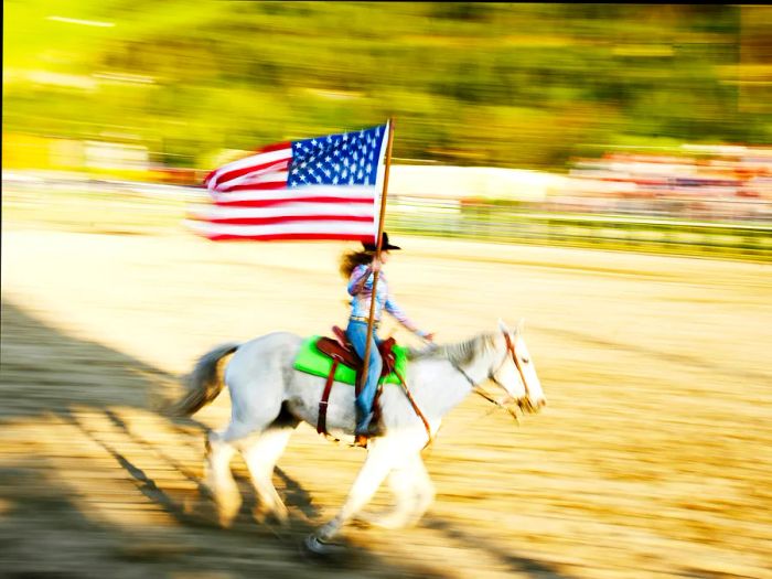 Woman riding horseback with an American flag at a rodeo