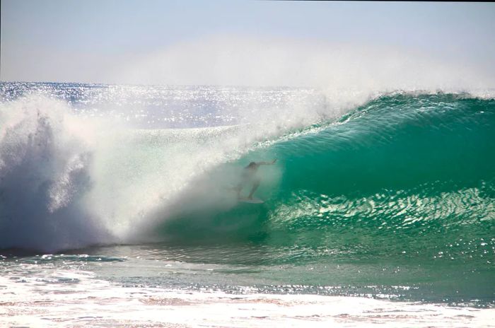 A surfer beneath a wave that arches overhead