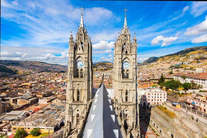 The twin spires of a cathedral tower over a hilly cityscape