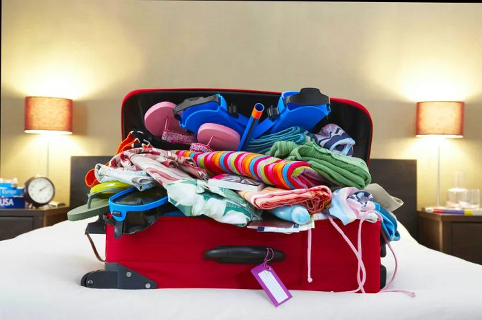 A suitcase overflowing with items on a bed