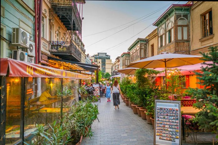 A charming narrow street in Tbilisi, lined with bars and restaurants featuring outdoor seating.