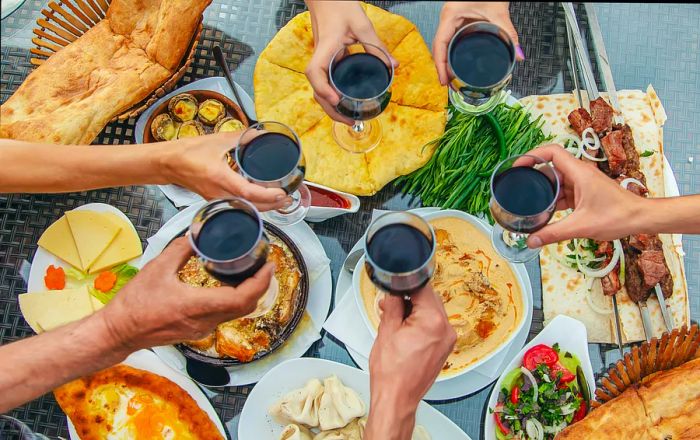 A group of six people toasting with glasses of red wine over a table filled with a variety of traditional Georgian dishes.