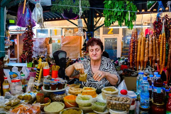 An elderly woman packages spices at a market stall in Kutaisi, Georgia.