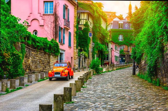 An orange Citroën 2CV cruises down a charming street in the Montmartre district of Paris.