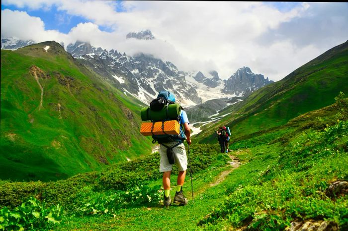 Hikers traverse a vibrant green trail in Svaneti, surrounded by the majestic peaks of the Caucasus mountains.