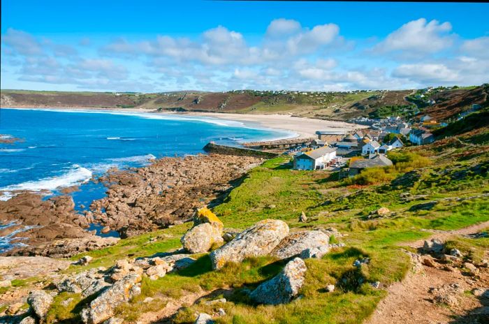 A broad sandy cove framed by rocky shores, dotted with white cottages along the cliffs.