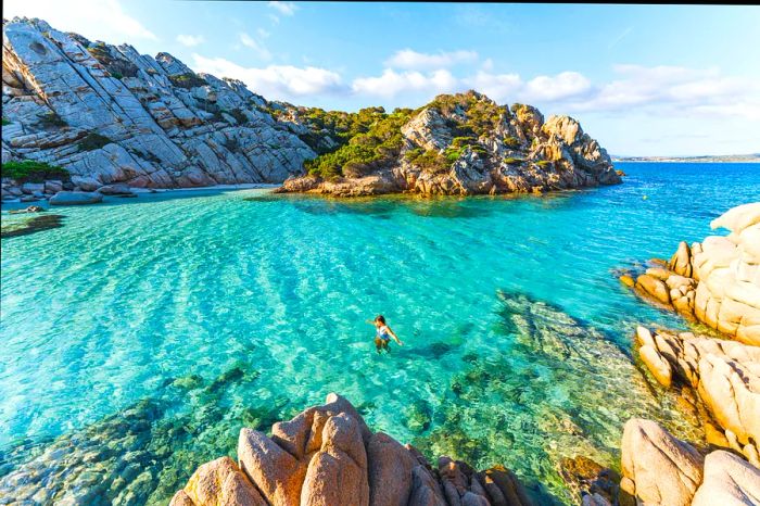 A person enjoys a swim in the tranquil waters of Cala Napoletana, Sardinia.