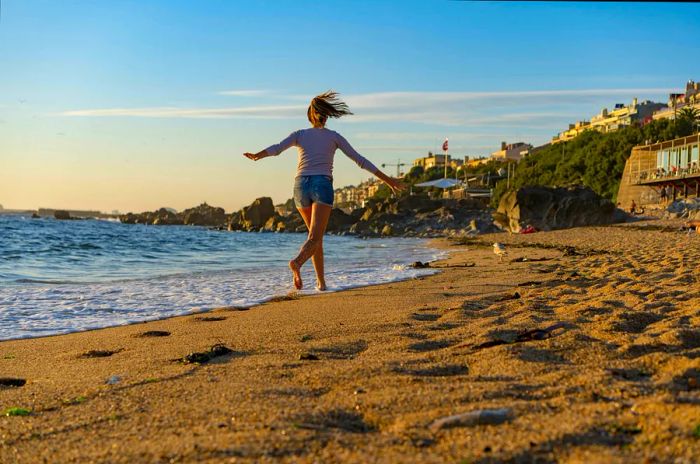 A young woman jogs along a sandy beach on a bright sunny day.