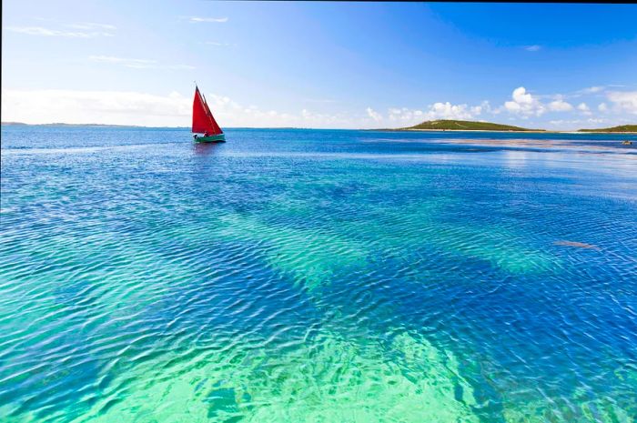 A yacht glides over turquoise waters.