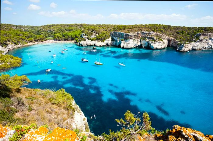 Bright blue waters off the coast of Menorca dotted with floating boats.