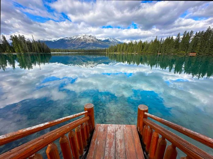 An alpine lake surrounded by trees perfectly reflecting a distant mountain