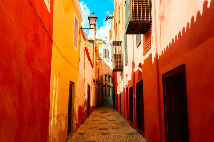 A vibrant alley adorned with buildings in shades of orange, yellow, and pink, Badajoz, Extremadura, Spain