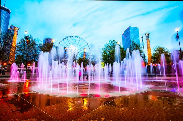 Fountains shaped like the Olympic Rings shoot water high into the air at Centennial Olympic Park as dusk falls.