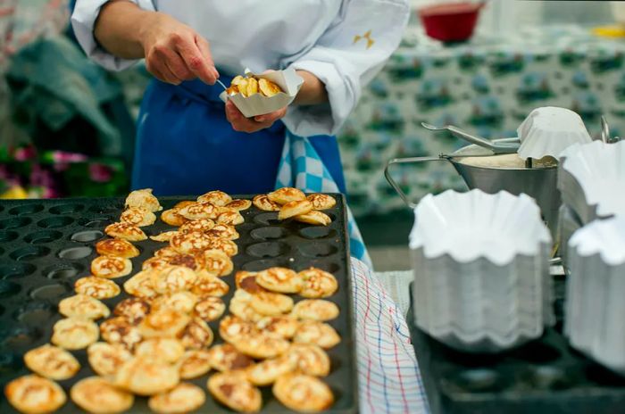 A chef serves small pancakes in a cardboard tray at a street market.