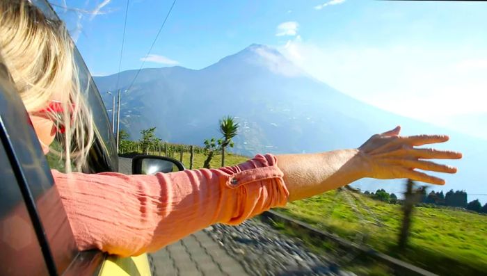 A woman extends her arm from a car window in Ecuador, with a mountain backdrop.