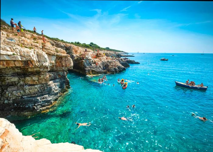 Boys leap into the sea from a cliff in Premantura, Croatia, Europe