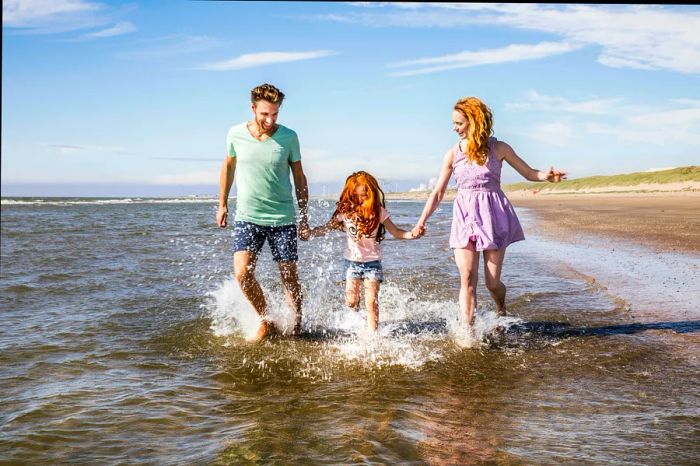 A family of three splashes through the shallow waters on a beach day