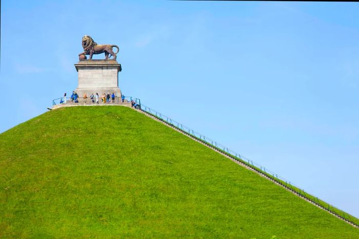 A grassy mound with steps leading to a large platform featuring an impressive bronze lion statue.