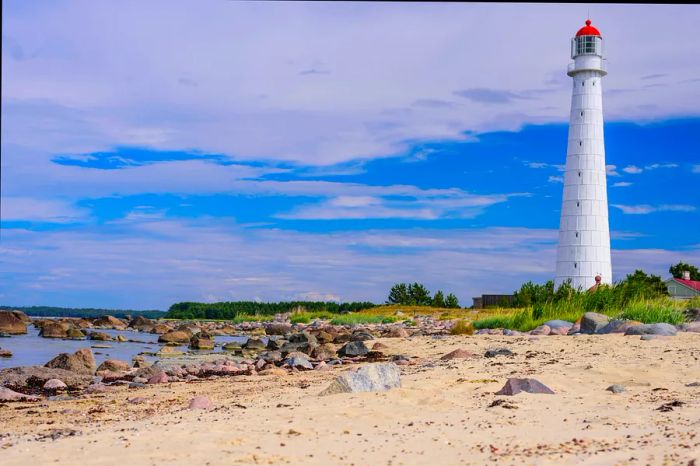 A tall white lighthouse standing on a secluded rocky and sandy beach