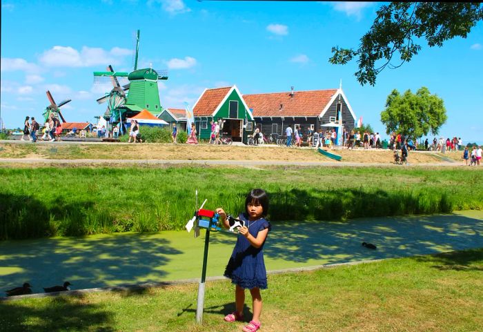 A girl plays with a toy windmill beside the authentic windmills of Zaanse Schans, Netherlands