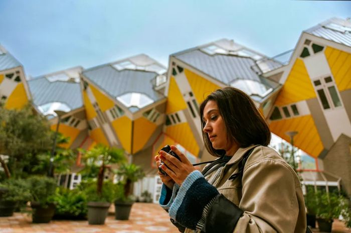 A woman captures the scene in front of the striking yellow cube-like houses of the Overblaak Development in Rotterdam, Netherlands