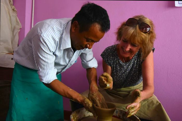 A teacher demonstrates to a student how to refine the edges of a pot on a pottery wheel.