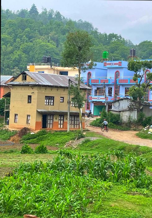 A cyclist pedals uphill amidst pastel-colored houses in a Nepali village