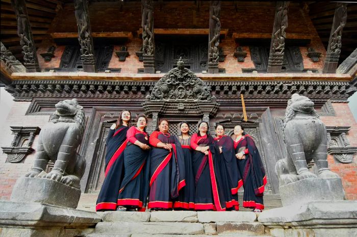 A group of women dressed in elegant black and red gowns stand in front of an intricately carved wooden door