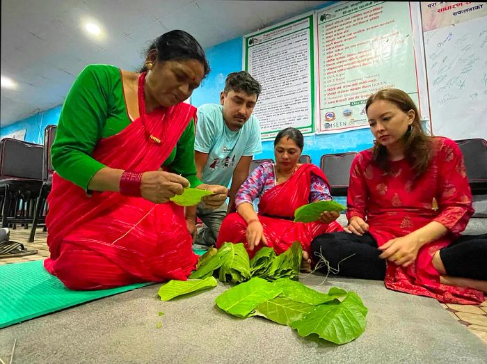 Two individuals demonstrate how to stitch large green leaves together to create a plate